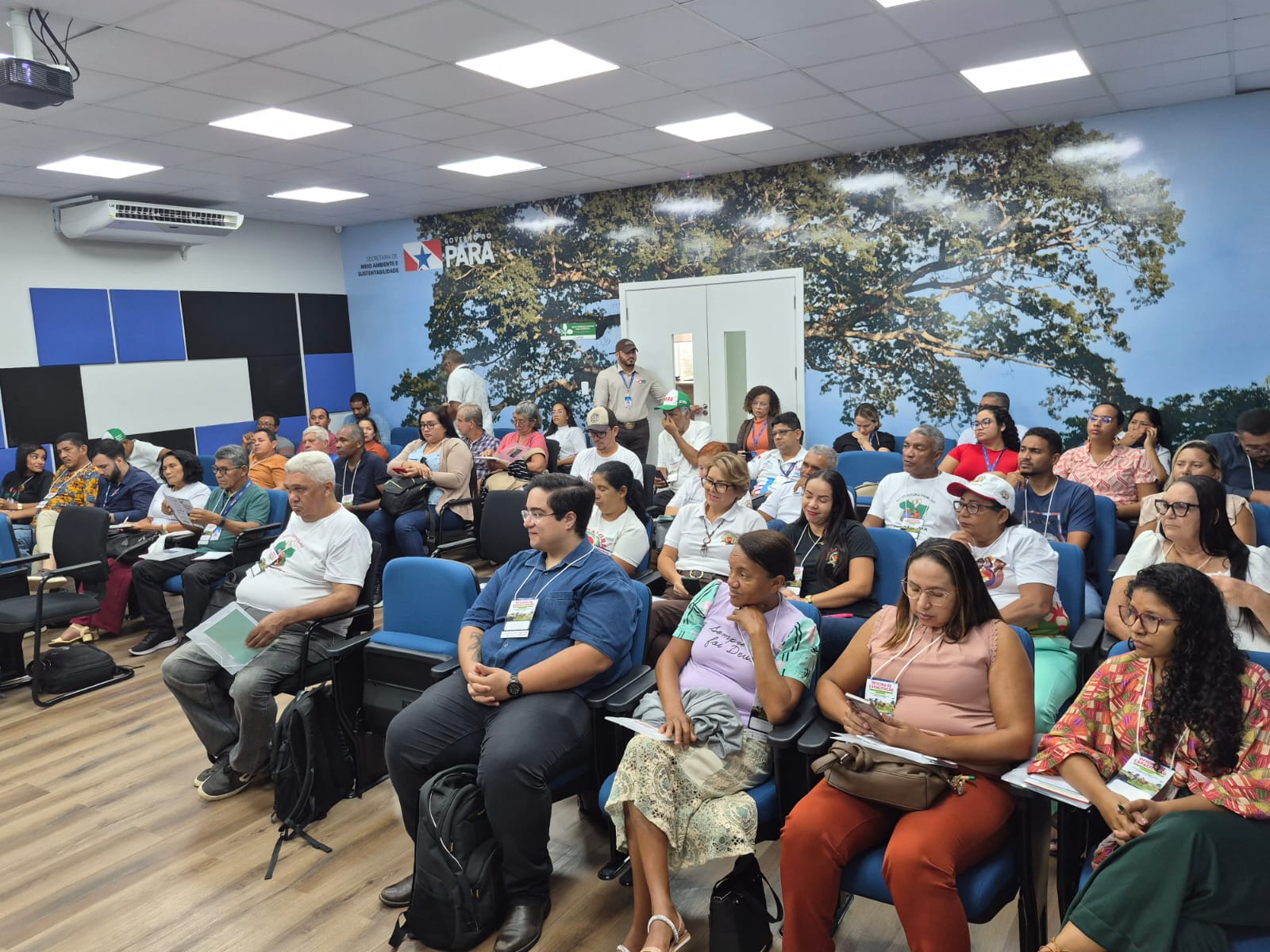 Imagem mostra público sentado em cadeiras de auditório, formado por homens e mulheres de diferentes biotipos 