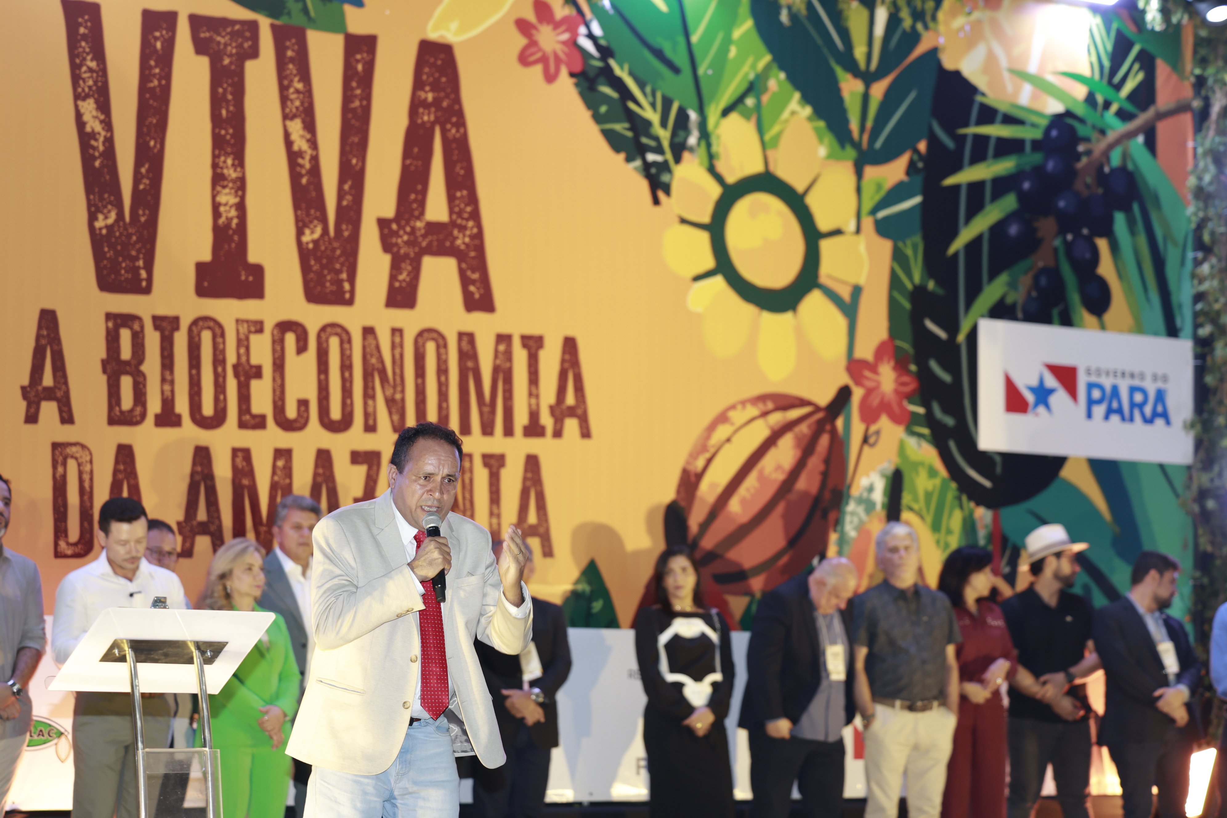 Imagem mostra homem ao microfone, em palco, falando para o público