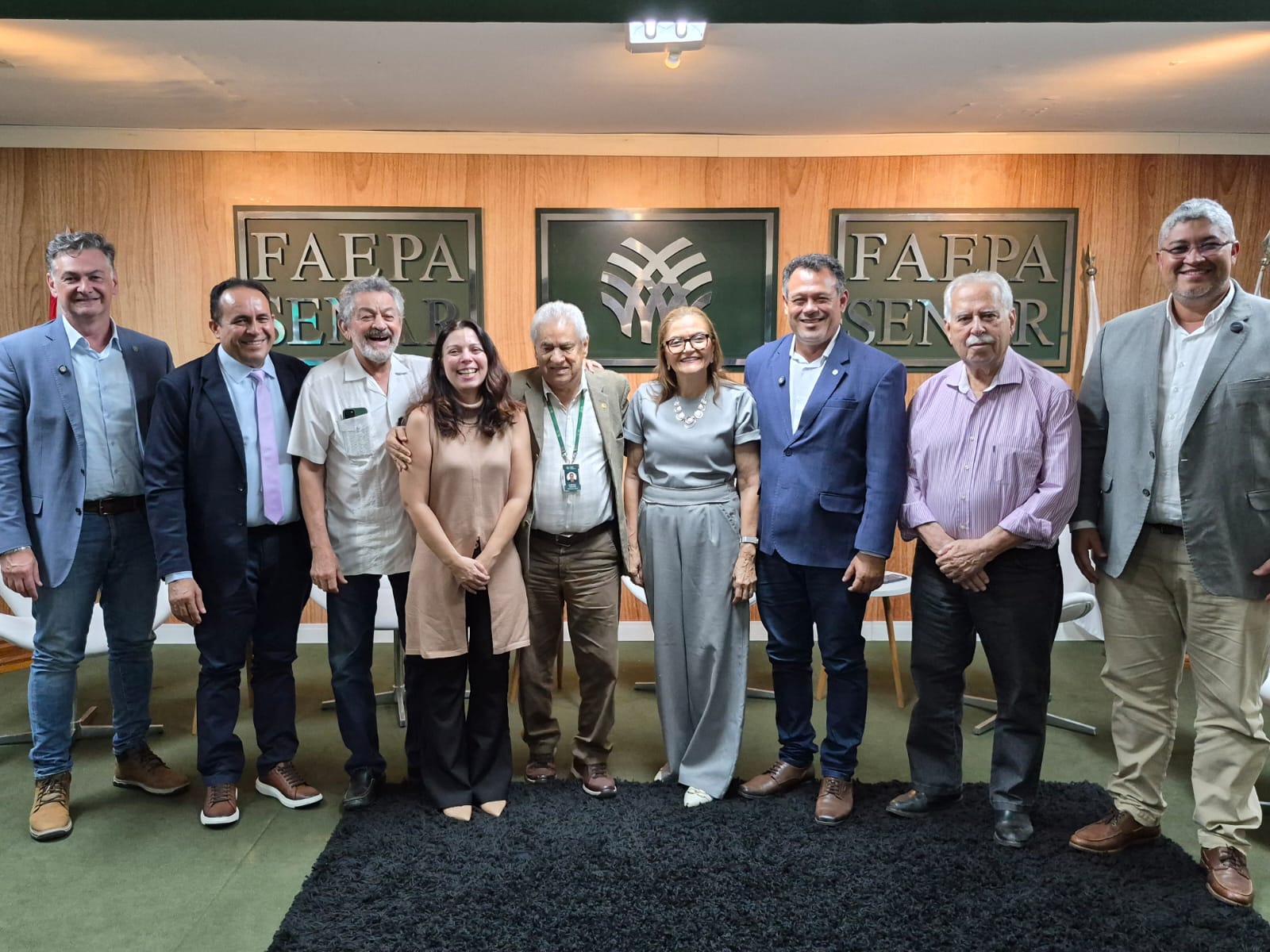 imagem mostra nove pessoas, 7 homens e duas mulheres, de pé, posando para foto em evento