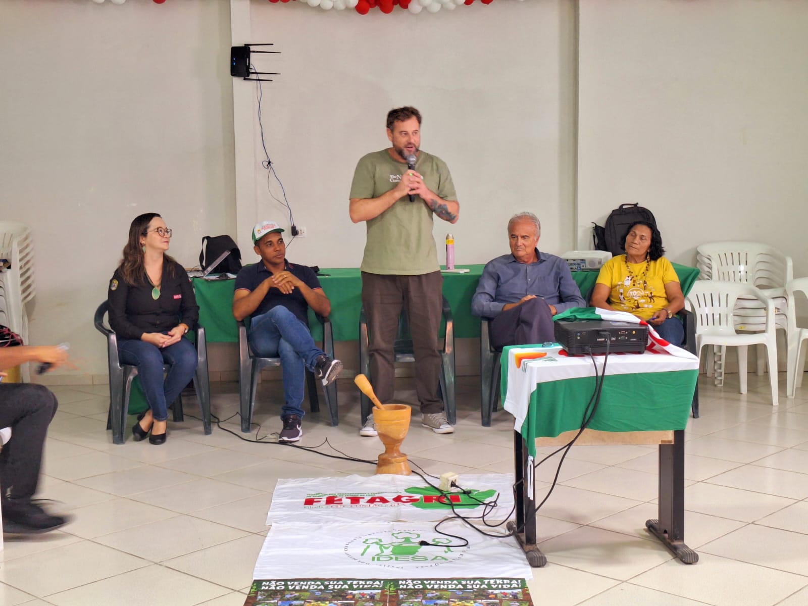 Homem de verde está de pé, ladeado de quatro pessoas sentadas em exposição