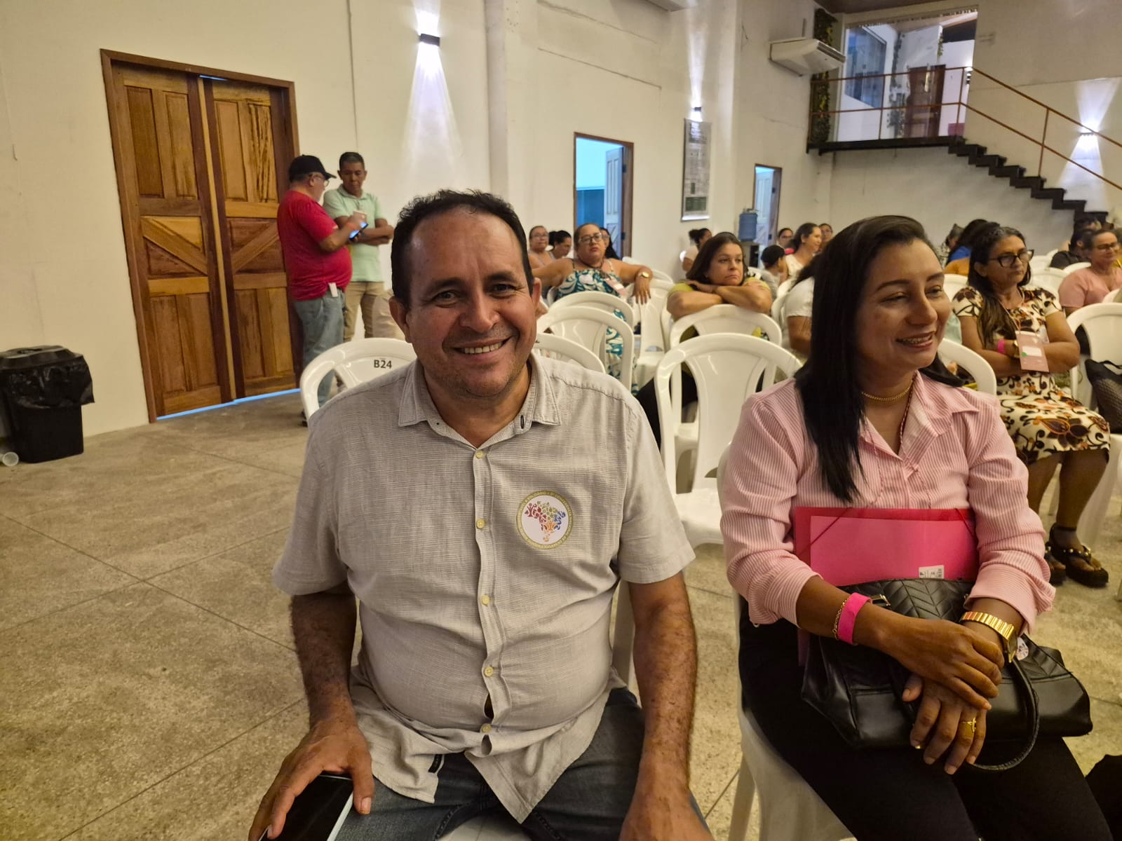 Imagem mostra pessoas sentadas eu auditório, com destaque para homem branco, sorrindo, de camisa clara e meia idade