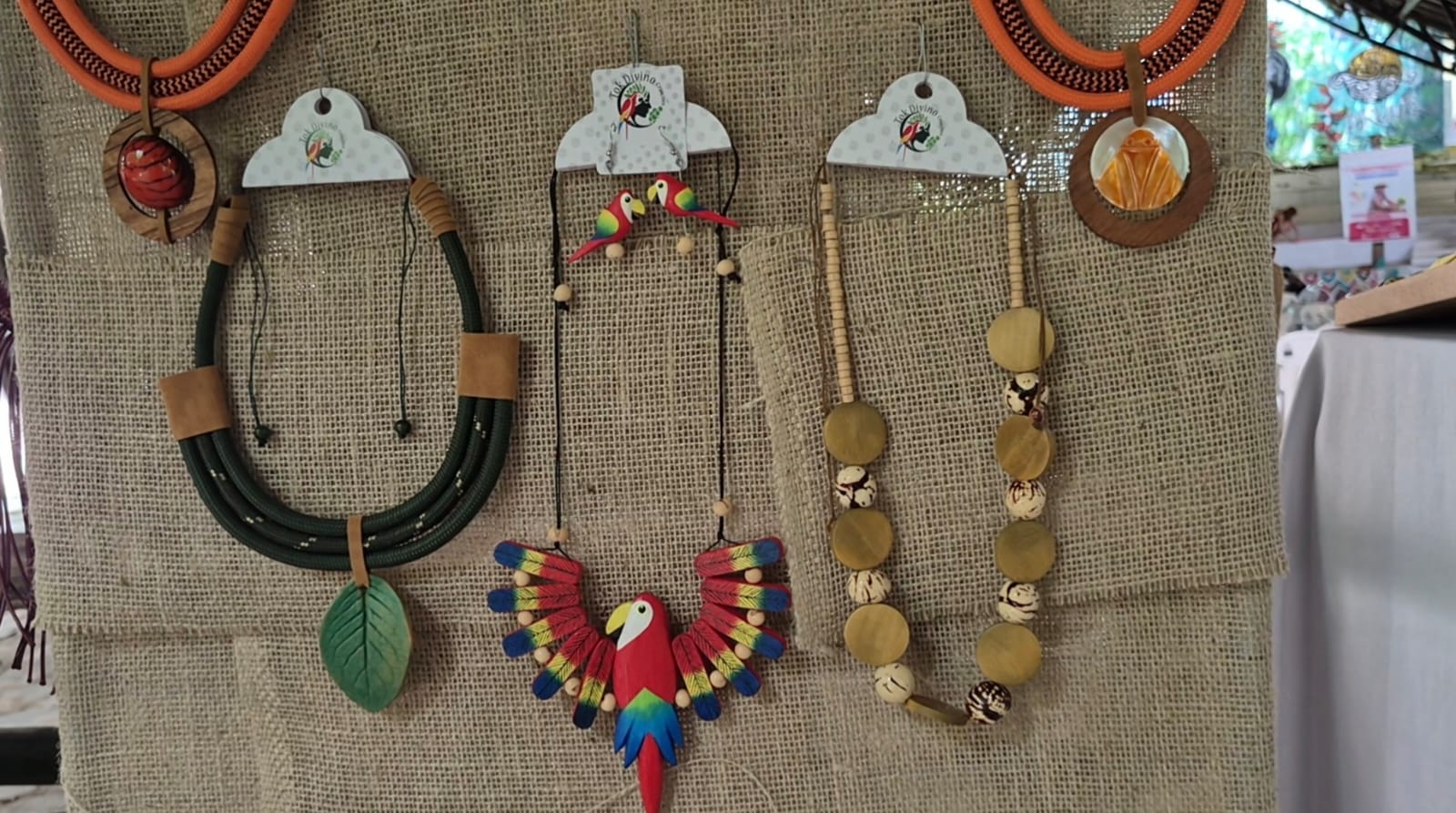 Imagem mostra colares artesanais expostos em tela de estopa, em feira de agricultura