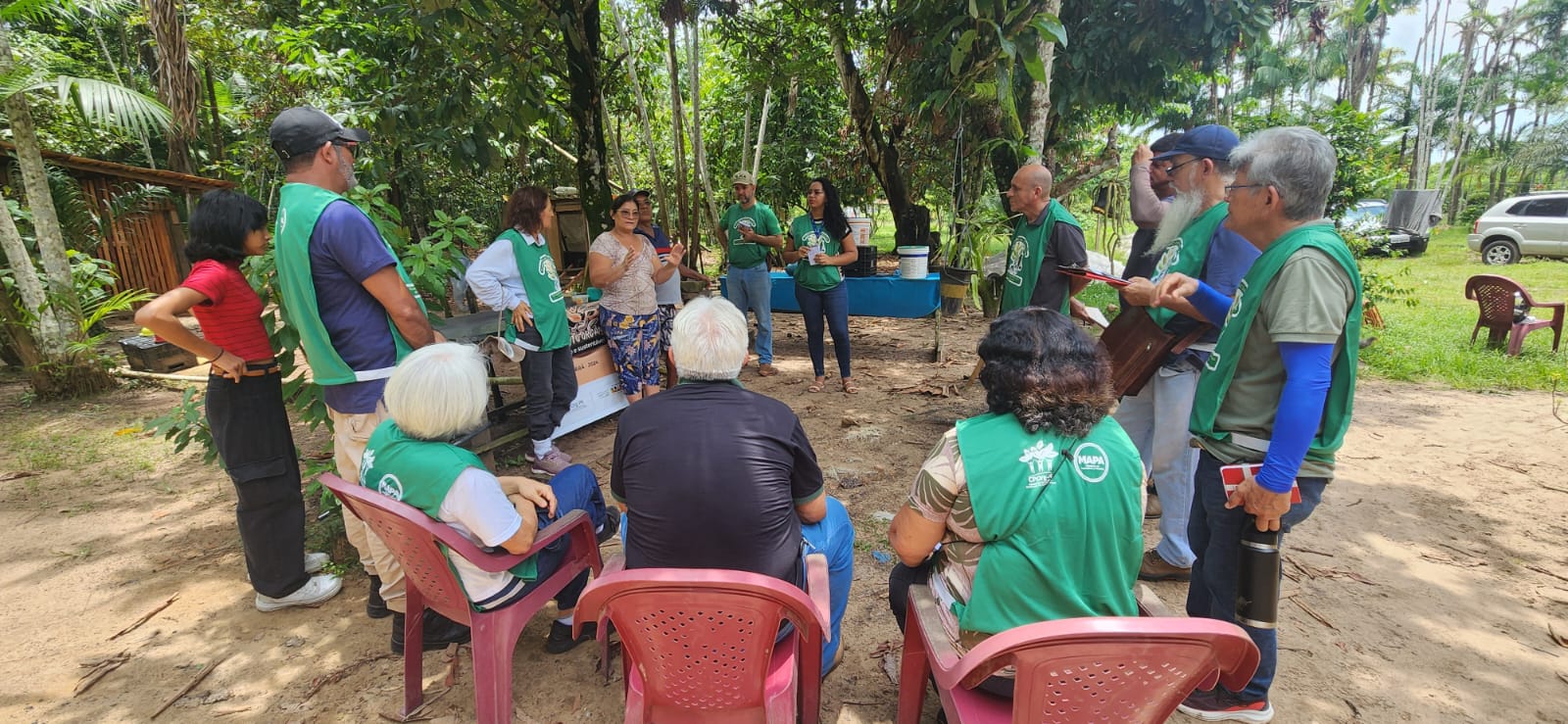 Imagem mostra grupo de pessoas reunidas em círculo, algumas sentadas e outras de pé, uma delas falando e gesticulando