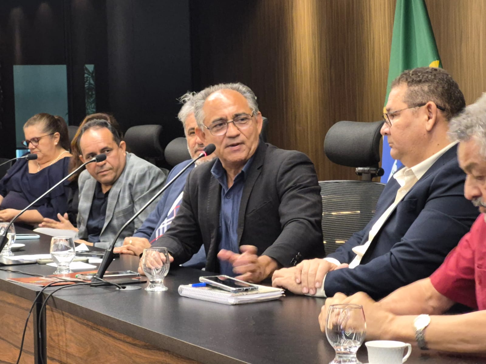 imagem mostra grupo à mesa com microfones