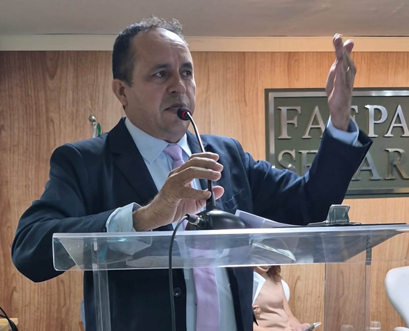 imagem mostra homem pardo, de terno preto e camisa clara, meia idade, discursando e gesticulando ao microfone