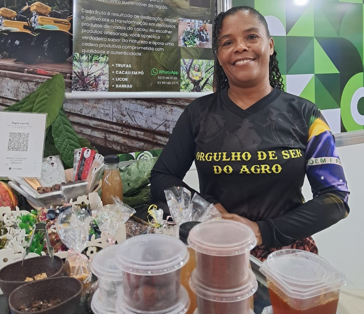 Imagem mostra mulher, negra, de camisa escura, posando ao lado de mesa cheia de doces de chocolate